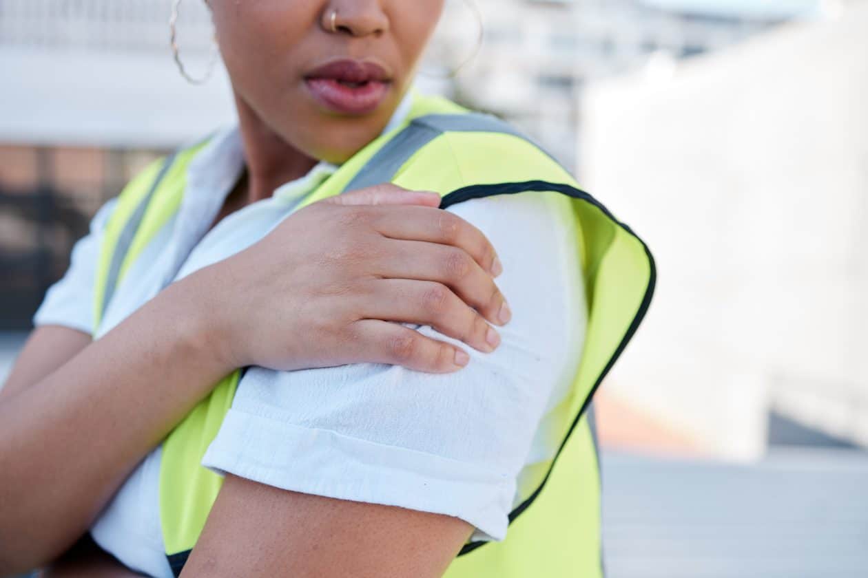 Mujer, ingeniera, con dolor en el hombro por una lesión, accidente o tensión muscular al aire libre en una azotea. Primer plano de una contratista con dolor en el brazo, malestar e inflamación en la articulación en el sitio de construcción